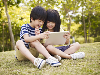 two asian children using tablet outdoors