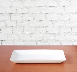 Empty plate on wood table over white brick wall background