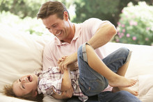 Father With Son Laughing Together On Sofa