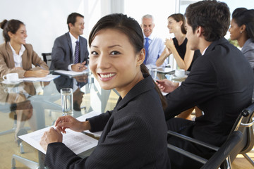 Wall Mural - Asian Businesswoman Sitting Around Boardroom Table With Colleagues