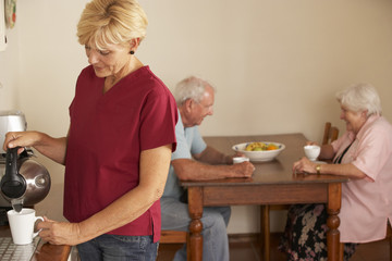 Poster - Home Help Sharing Cup Of Tea With Senior Couple In Kitchen