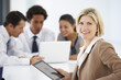 © Monkey Business - Portrait Of Female Executive Using Tablet Computer With Office Meeting In Background