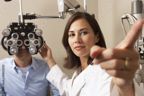 Fotografía Female Optician In Surgery Giving Man Eye Test
