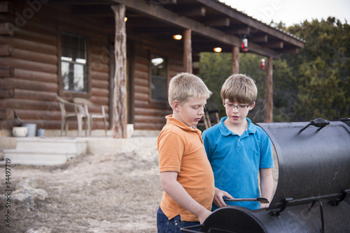 Fotografie, Obraz Twoboys grilling sausages at barbecue pit