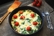 Frittata (italian omelet) with cherry tomatoes and spinach in pan on linen cloth. Angle view