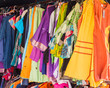 © dinax - Ropas alegres / Vestidos de colores brillantes colgados en un mercadillo