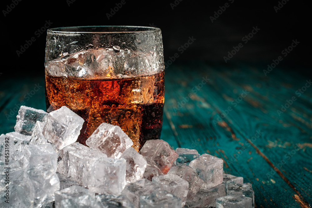 Glass of cola with ice on a wooden table. - obrazy, fototapety, plakaty 