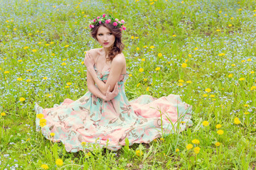 beautiful sexy tender girl in a summer sundress and with a wreath on his head sitting in the meadow of blue flowers