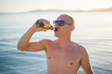 young handsome sporty man drinking beer at the beach sunset