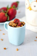Delicious homemade granola with dried fruits in tiny princess blue cup. Fresh strawberries on background