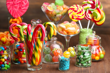 Wall Mural - Colorful candies in jars on table on wooden background