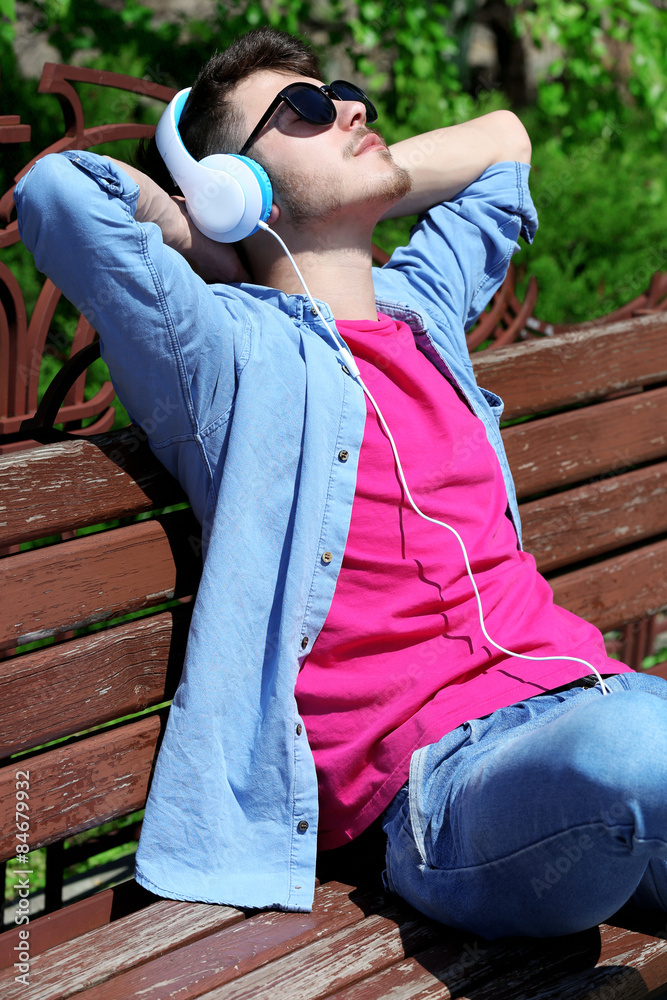 Man with headphones resting on bench in park