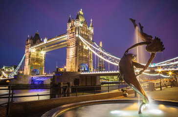 Wall Mural - London, United Kingdom - The lady and the dolphin fountain with the iconic illuminated Tower Bridge at night