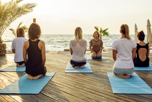 Group Of Young Females Practicing Yoga On The Seaside During The Sunrisе