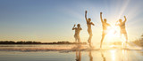 Glückliche junge Menschen laufen und springen am See beim Sonnenuntergang