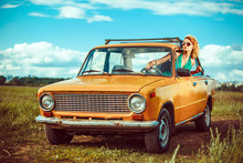 Woman Is Driving An Old Yellow Car. Rural Background.