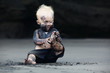Funny portrait of smiling child with dirty face sitting and playing with fun on black sand sea beach before swimming in ocean. Family active lifestyle, and water leisure on summer vacation with baby