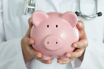 Female Doctor Holding Piggy Bank.