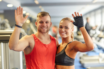 smiling man and woman waving hands in gym