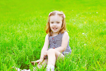 Portrait of little smiling girl child on the grass in sunny summ