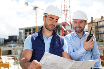 Wall Mural - Engineer and worker watching blueprint on construction site