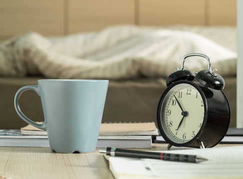 Cup mug and  retro alarm clock on the table in bedroom.