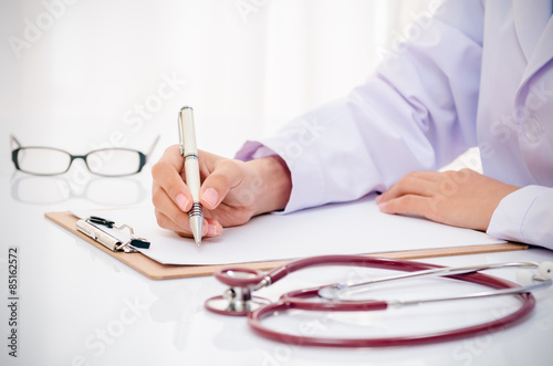 Fotografía Escritura del doctor de registro en la carpeta en el escritorio en la oficina