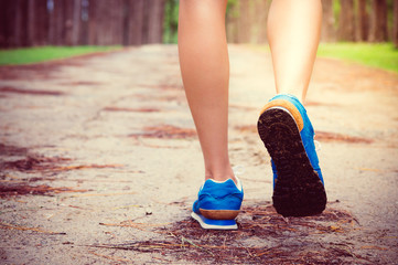 Women's running through pine tree forest trail.