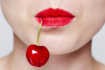 woman's face with red lipstick and a cherry hanging from the mouth