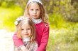 Two little sisters posing outdoors over nature background. Holding each other. Smiling girls.