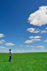 Wall Mural - young man looks at the bright sky over the green field