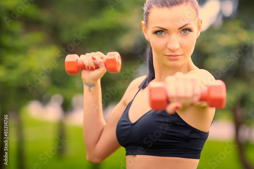 Fotografie, Obraz Female fitness instructor exercising with small weights in green