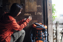 Austria, Altenmarkt-Zauchensee, Young Female Hiker Carving Her Name In Wooden Door Of Alpine Cabin