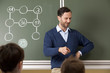 © Westend61 - Smiling teacher at blackboard with arithmetic problem