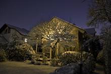 Germany, Lighted One-family House With Snow-covered Garden In The Foreground