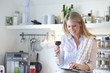 © Westend61 - Smiling woman in kitchen drinking glass of red wine and using digital tablet