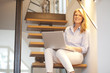 © Westend61 - Smiling woman using laptop on stairs