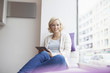 © Westend61 - Portrait of smiling woman with digital tablet sitting at window