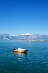 Wall Mural - Small fishing boat with snow covered mountains in Antalya Turkey