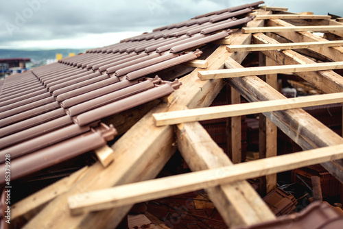 Fotografie, Obraz Roof under construction with stacks of brown, modern tiles covering house