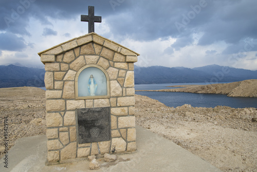 Fotografie, Obraz Marienfigur auf der Insel Pag mit dramatischem Himmel vor dem Velebit Gebirge