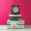 Alarm clock with polka dots boxes over pink modern background. Glamour feminine objects