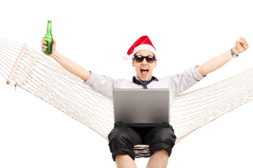 Poster - Joyful guy with Santa hat working on a laptop seated in a hammoc