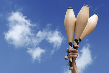 man's hand holding three wooden juggling clubs in the blue sky