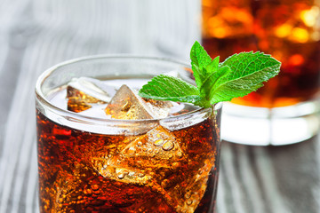 Two glasses of cola with ice and fresh mint on wooden table.