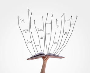 Human hand holding book with flying math formulas