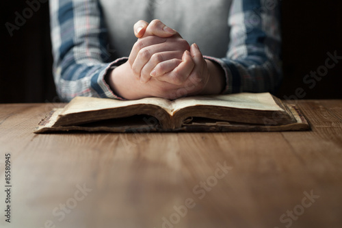 Fotografie, Obraz Woman hands praying with a bible in a dark over wooden table