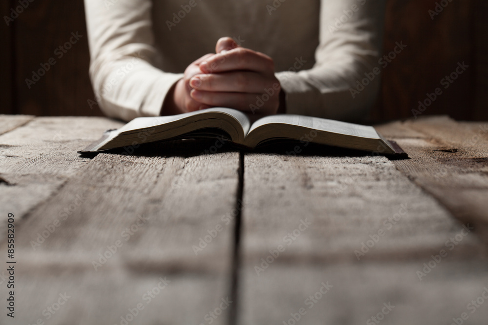 Woman hands praying with a bible in a dark over wooden table - obrazy, fototapety, plakaty 