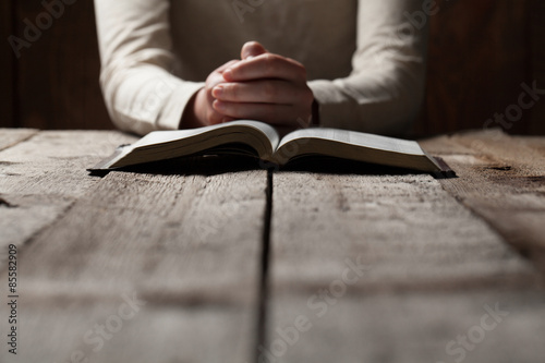 Cuadros en Lienzo Manos de la mujer que ruega con una biblia en una mesa de madera oscura sobre