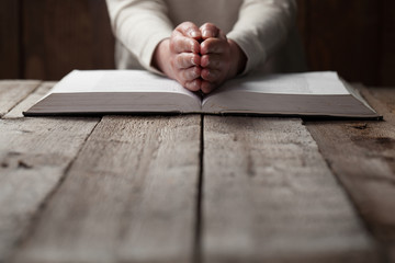 Wall Mural - woman hands on bible. she is reading and praying over bible in a dark space over wooden table